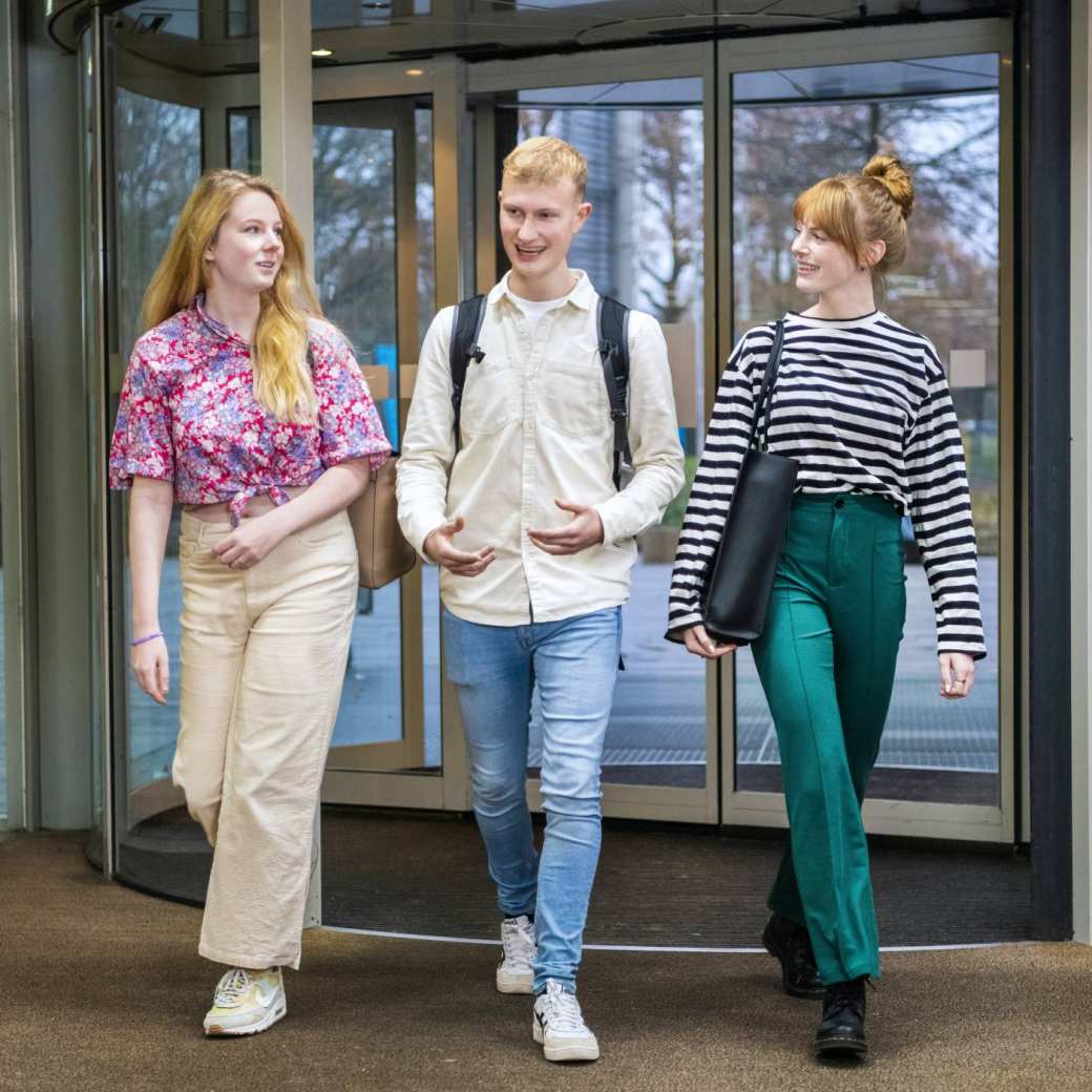 Drie studenten wandelen de school binnen. 