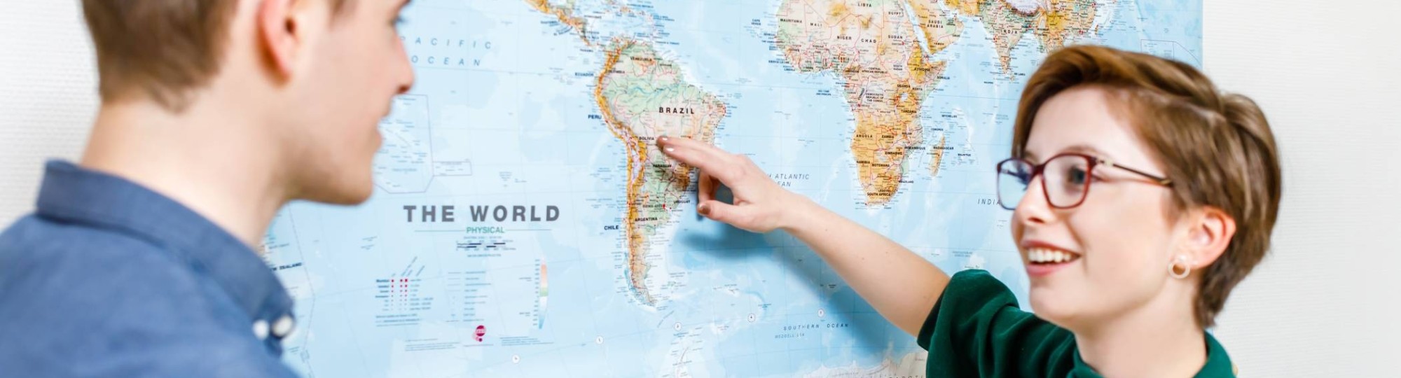 Studente Leraar Aardrijkskunde wijst Zuid-Amerika aan op de wereldkaart die aan de muur hangt.