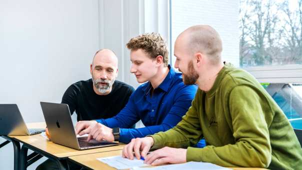 3 mannelijke studenten met laptop overleggen met elkaar tijdens les