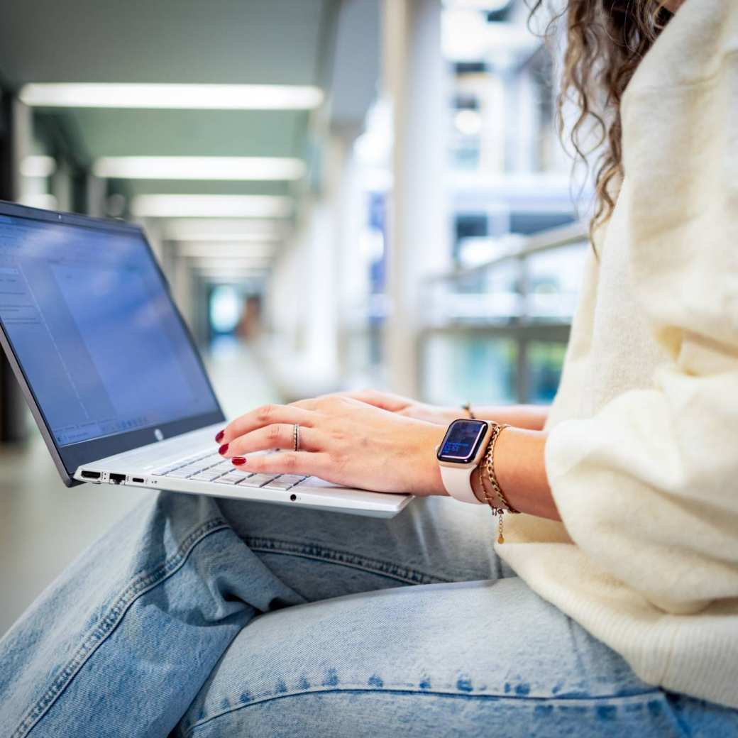 Student van de bachelor Commerciële Economie deeltijd, duaal in gang met laptop.