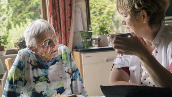 een thuiszorgverpleegkundige helpt een nog thuiswonende oudere dame met beginnende dementie bij de dagelijkse zorgtaken