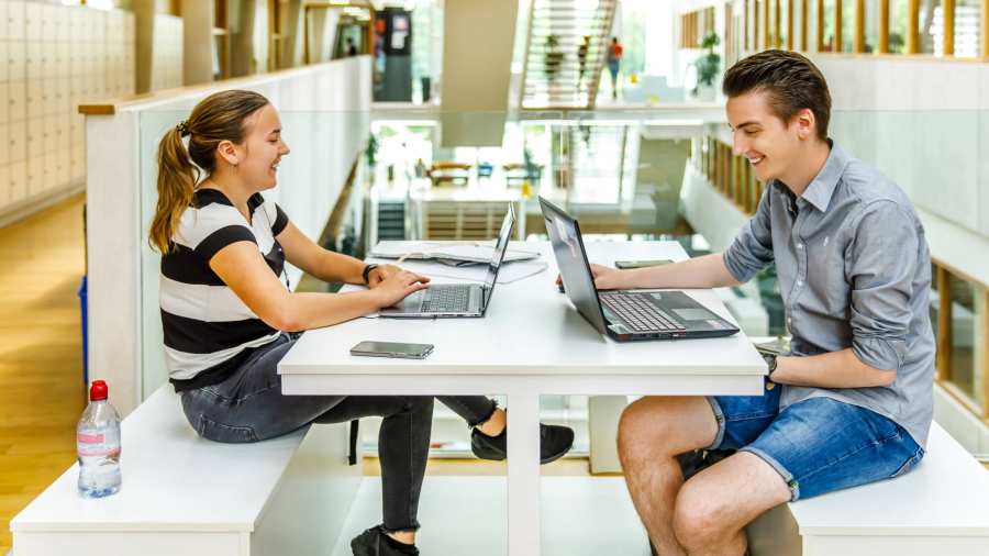 Jongen en meisje studeren samen op laptop in grote hal