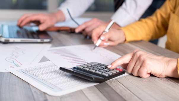 Foto van rekenmachine, vier handen en een laptop voor projectpagina Associate lectoraat Sustainable Finance & Tax