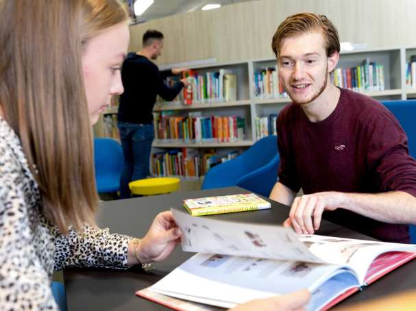 Studenten HAN Pabo Arnhem bladeren in boek in bibliotheek.