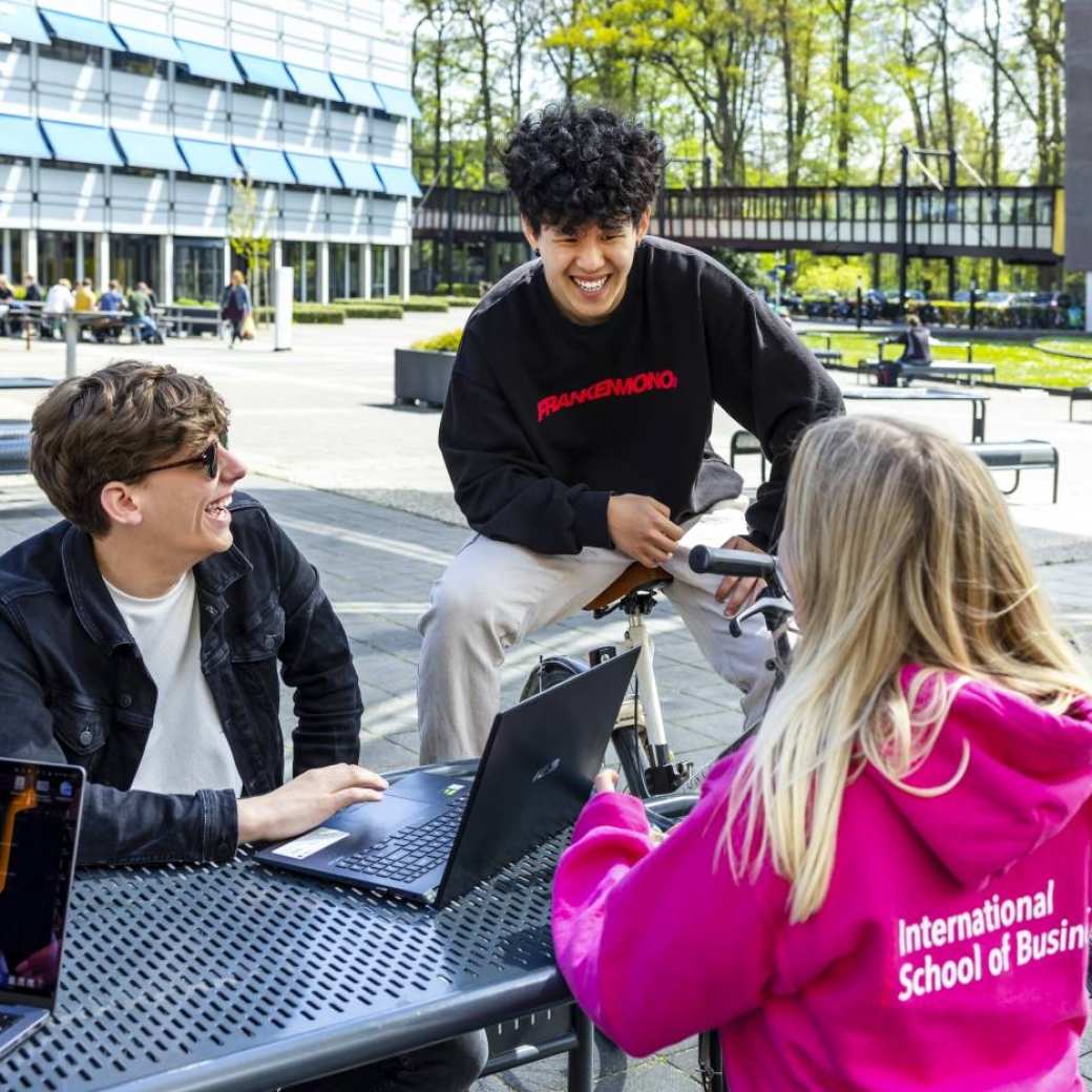 3 studenten in gesprek met elkaar buiten aan een tafel R31