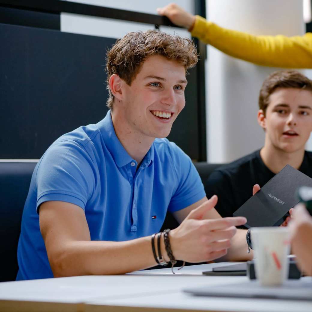 HBO-ICT studenten kijken lachend naar hun laptop met een docent op de achtergrond