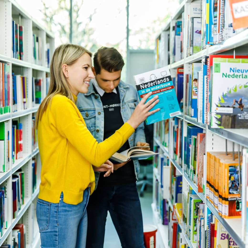 Twee studenten Leraar Nederlanders zijn op zoek naar een boek in de bibliotheek. 