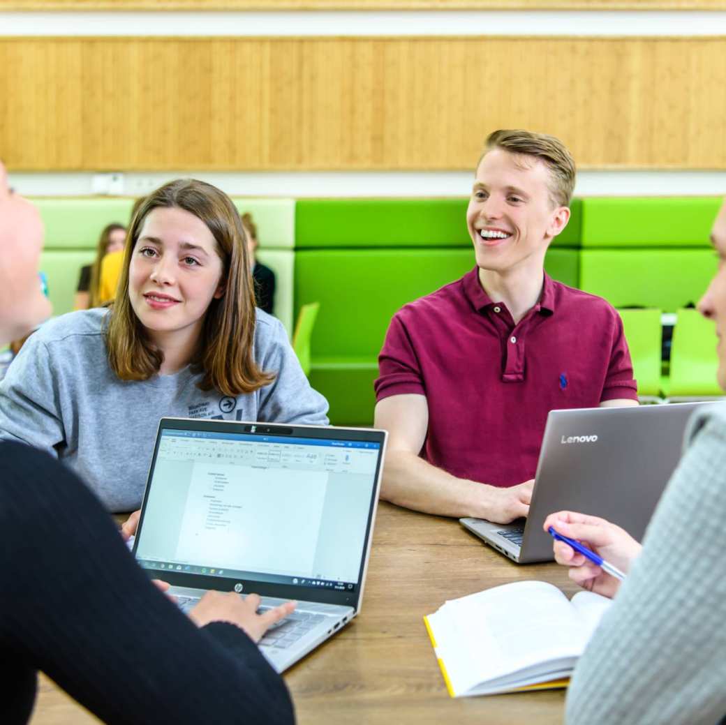Vier studenten Leraar Duits werken in een klaslokaal aan tafel met laptops