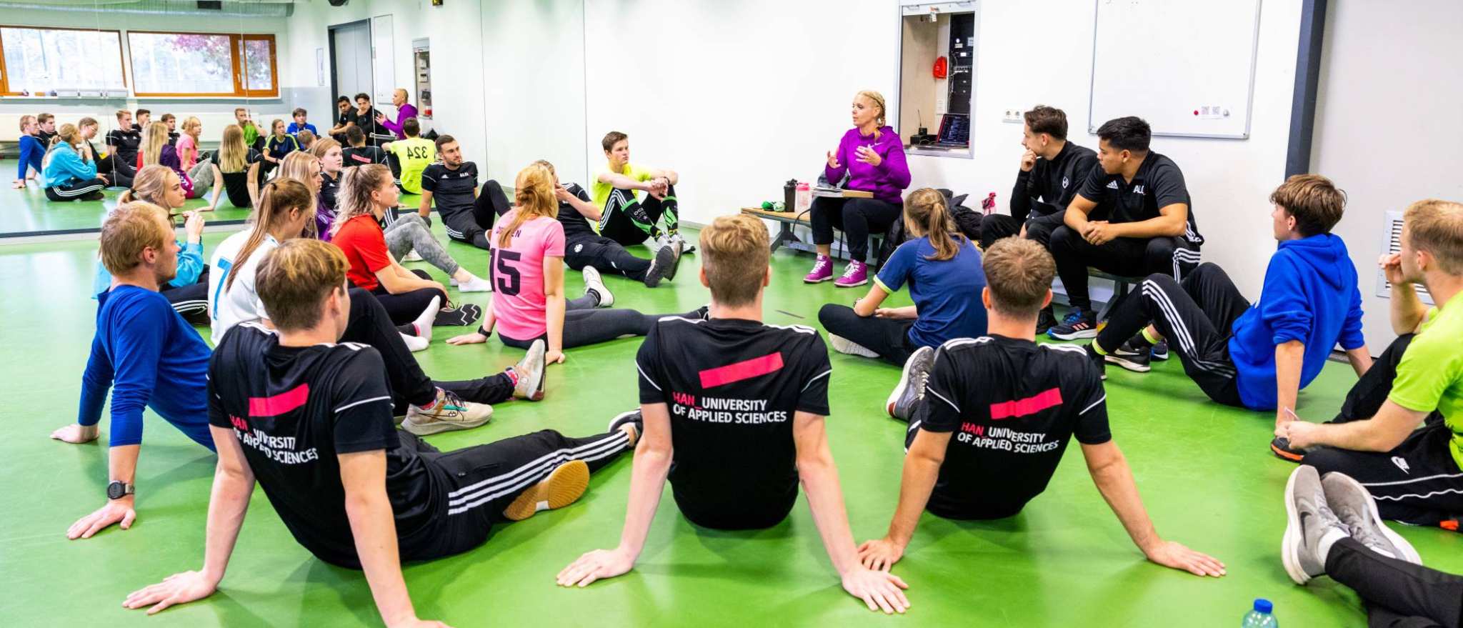Studenten luisteren in de sportles naar docente.
