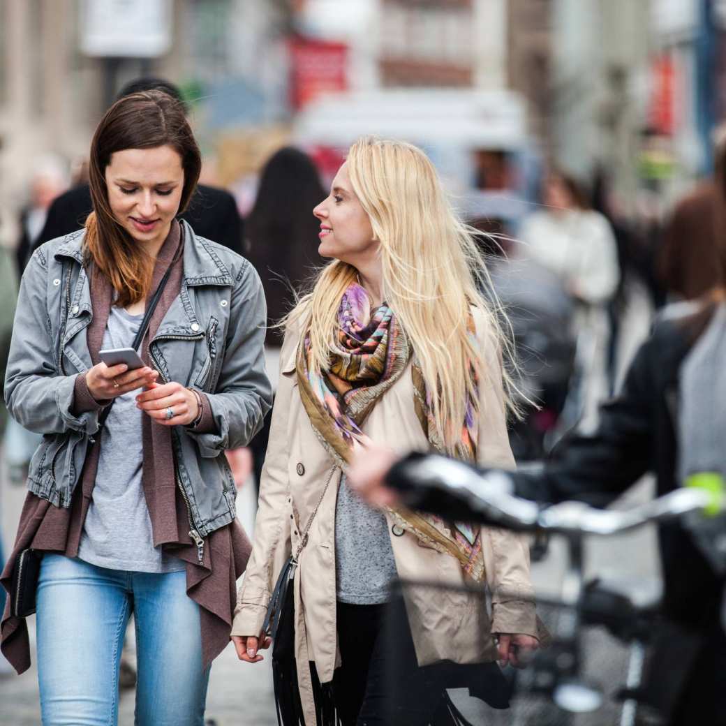 237749 vrouwen lopend door de stad, eentje met fiets, eentje met mobiel