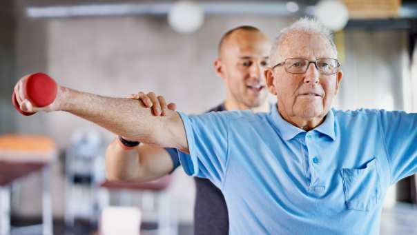 109963 fysiotherapeut die een oudere man met gewichten helpt