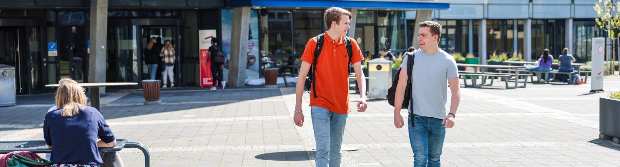 Twee studenten lopen lachend buiten op het plein voor de campus in Arnhem