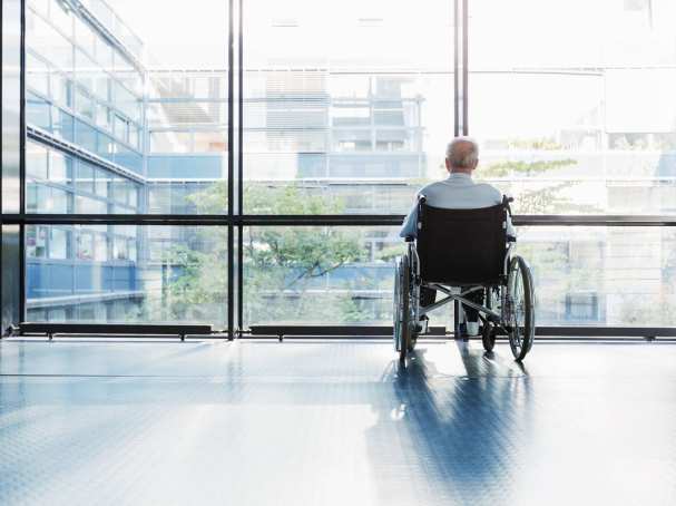 109943 oudere man in rolstoel kijkt uit raam in een het ziekenhuisgang