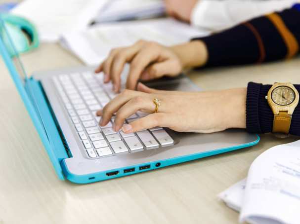 Twee vrouwenhanden typen op het toetsenbord van haar laptop.
