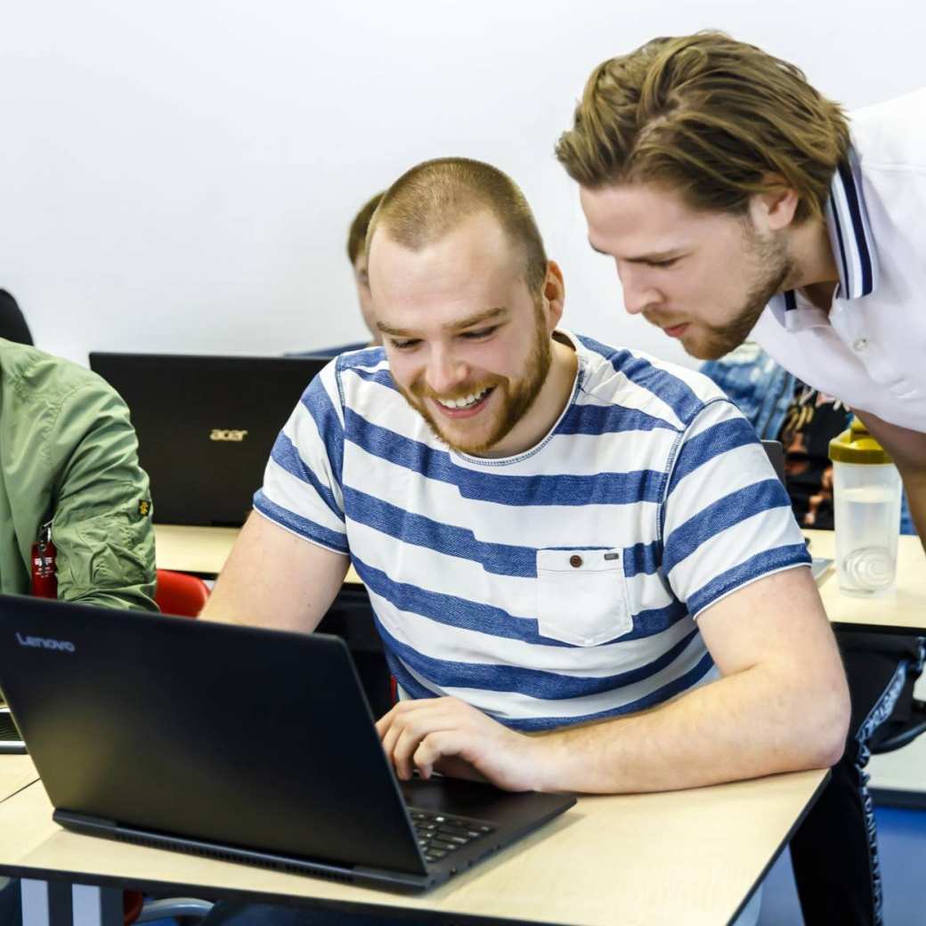 Twee HAN duaal studenten kijken samen naar een opdracht op de laptop tijdens hun college Commerciële Economie.