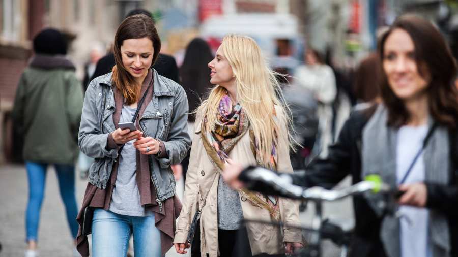vrouwen lopend door de stad, eentje met fiets, eentje met mobiel