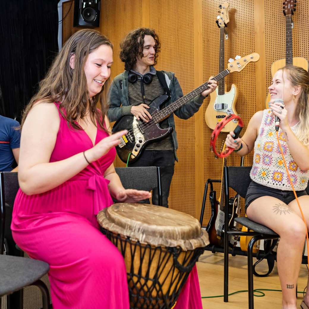 Muziektherapie studenten maken samen muziek tijdens een praktijkles. Een samenspel van gitaar, trommel en zang.