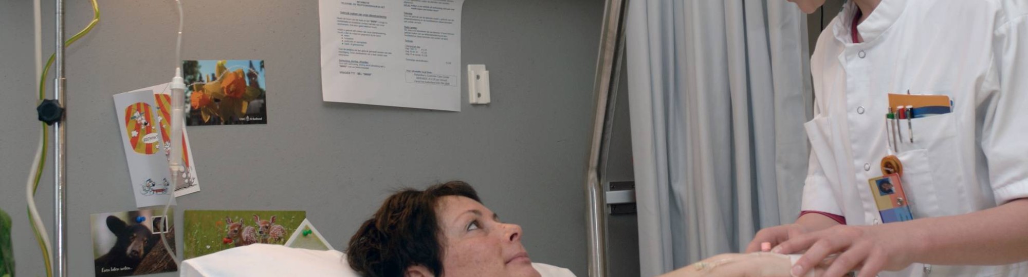 verpleegkundige inspecteert infuus bij patiente en maakt een praatje