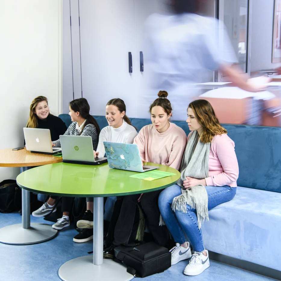 Verpleegkunde studentes werken samen op hun laptops tussen hun lessen door.
