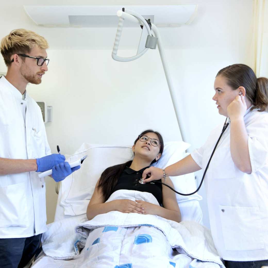 Studenten Medische Hulpverlening controleren hartslag patiënt en overleggen aan het bed