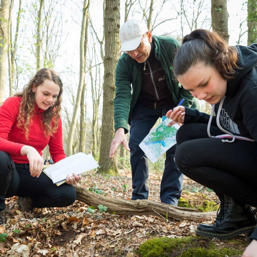 Studenten Leraar Biologie onderzoeken de grond in het bos met behulp van een kaart.