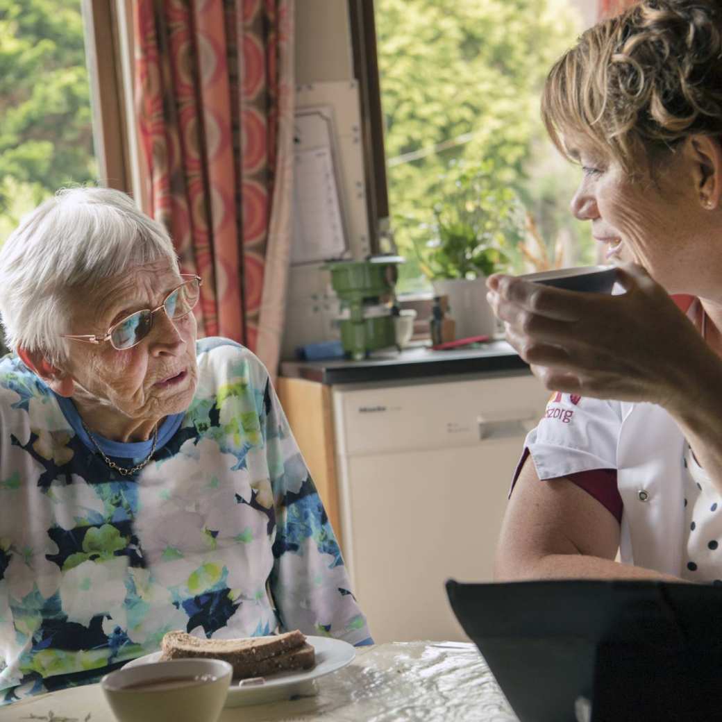 een thuiszorgverpleegkundige helpt een nog thuiswonende oudere dame met beginnende dementie bij de dagelijkse zorgtaken