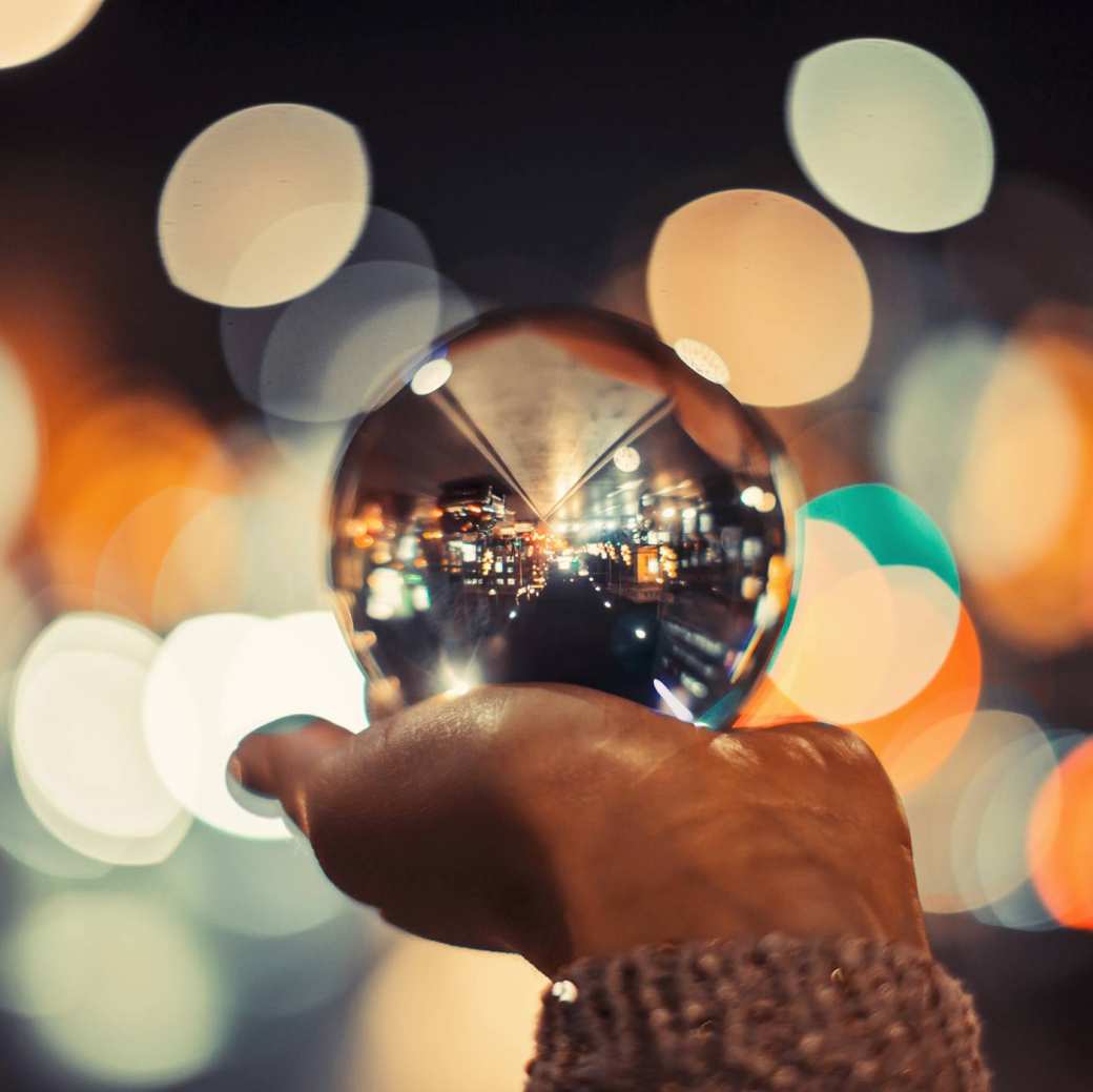 539125 Een glazen bol met een stad op een hand met kleurige achtergrond lichtjes