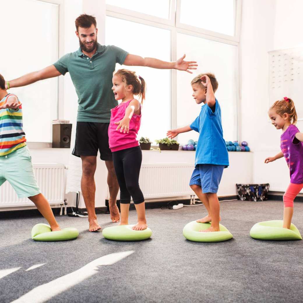 kinderen wandelen op pilates-ballen tijdens training op sportschool met mannelijke coach