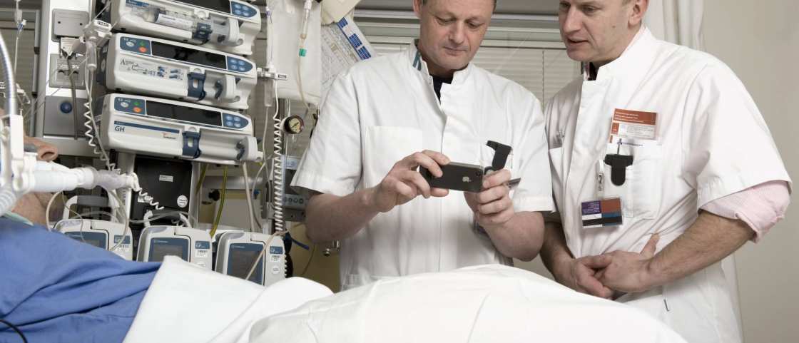 102262 2 mannen verpleegkundigen bekijken app op mobieltje aan bed IC