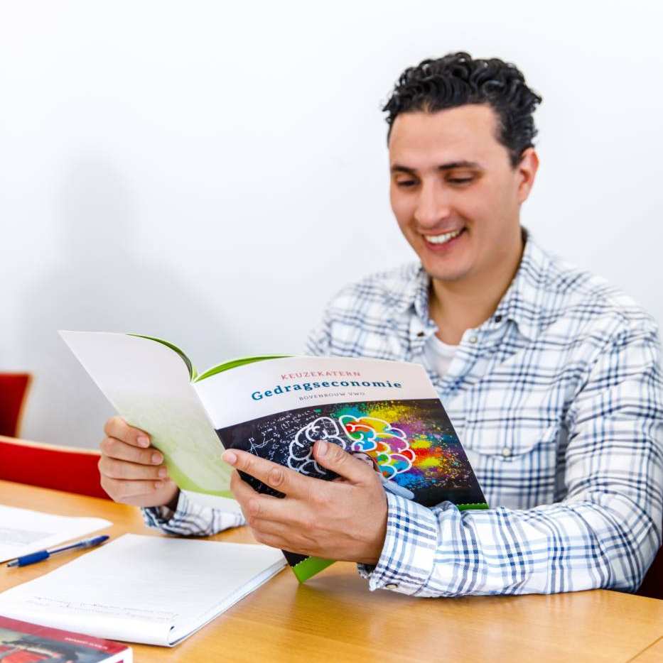 masterstudent kijkt lachend in een studieboek.