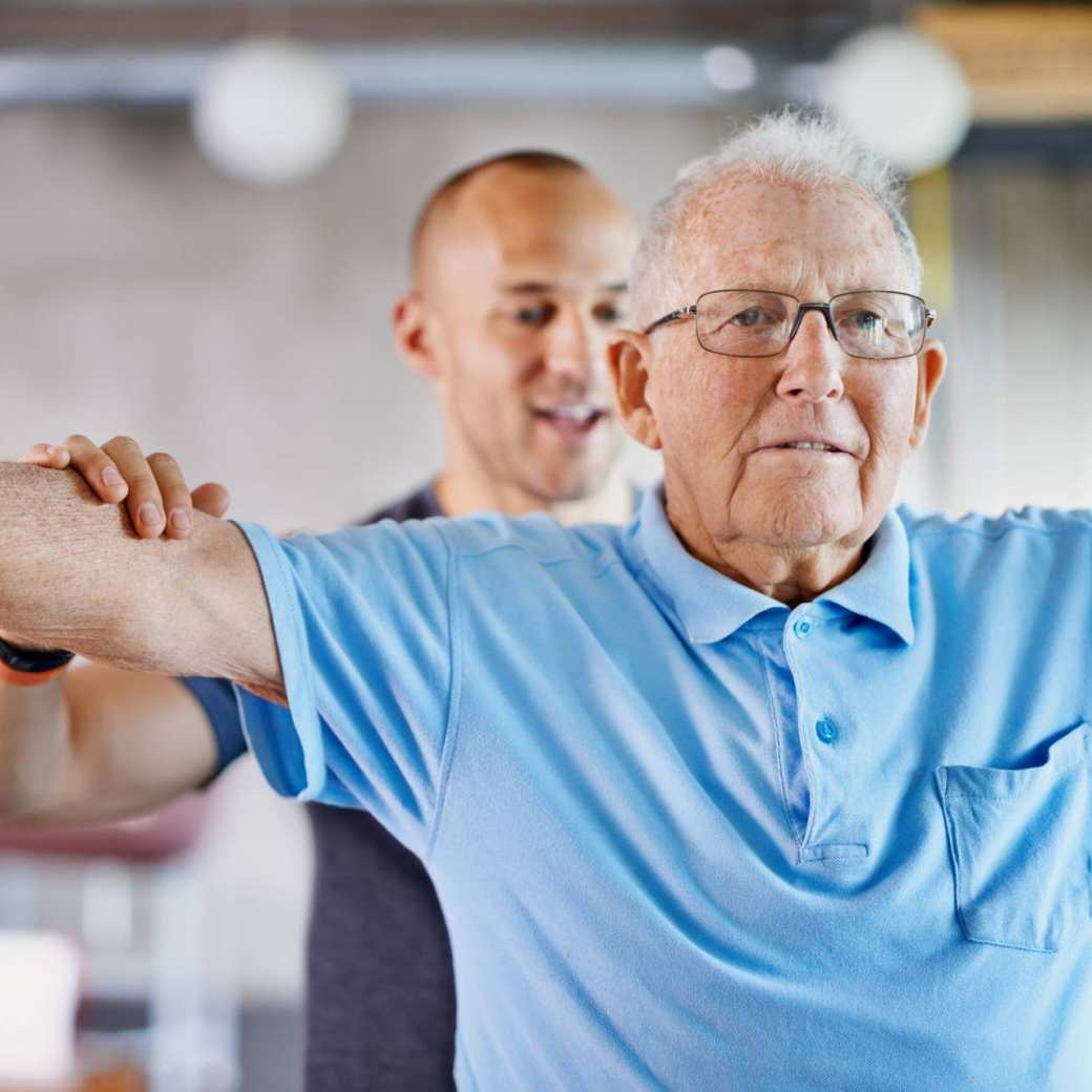 fysiotherapeut die een oudere man met gewichten helpt
