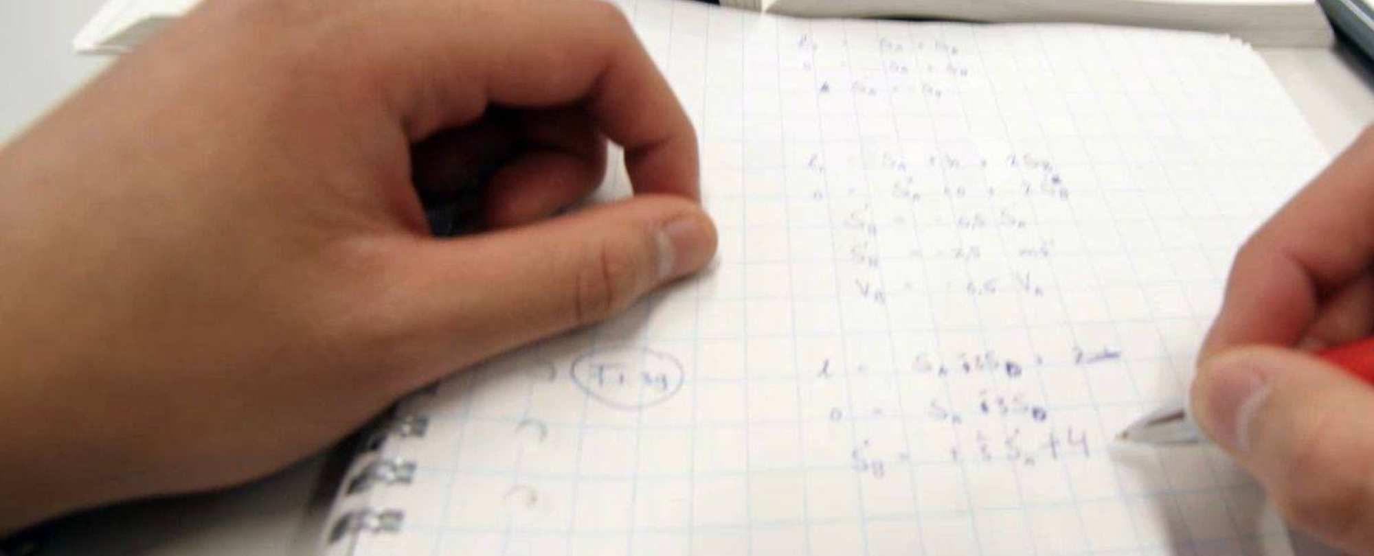 student maakt berekeningen met penen papier
