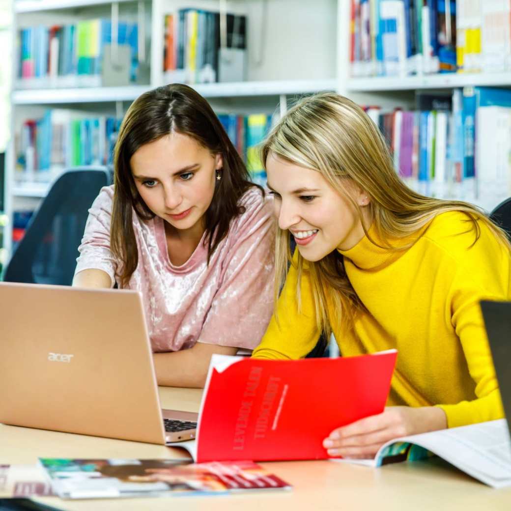 Twee studentes van de HAN kijken samen op een laptop in een studieruimte terwijl ze huiswerk maken