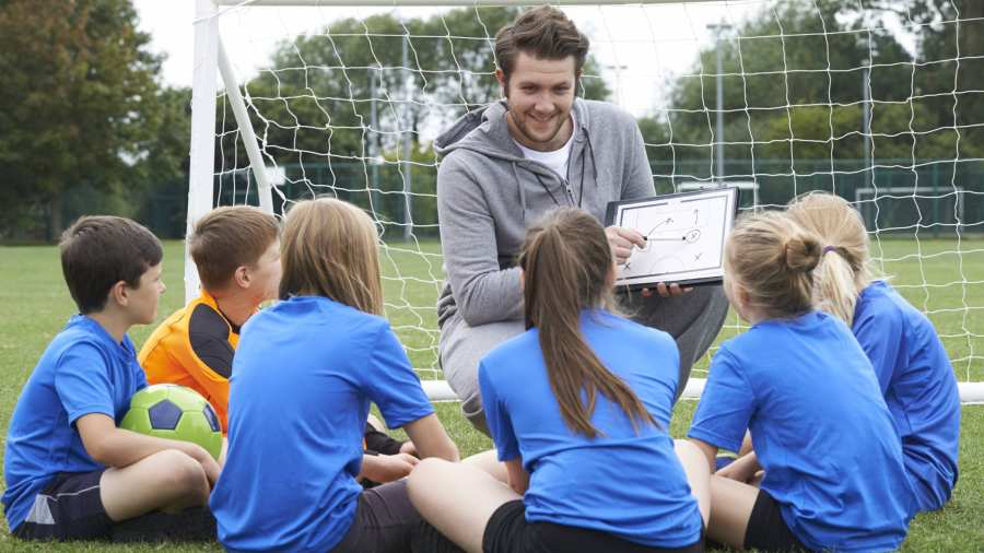 sportleraar geeft team met basisschool voetbalteam instructie 