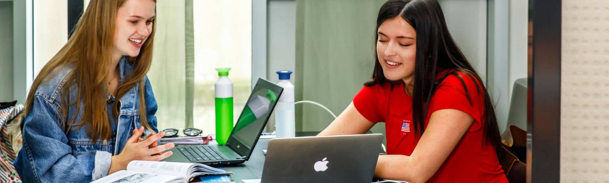 Twee meiden studeren samen met boeken en laptop een meisje rood shirt