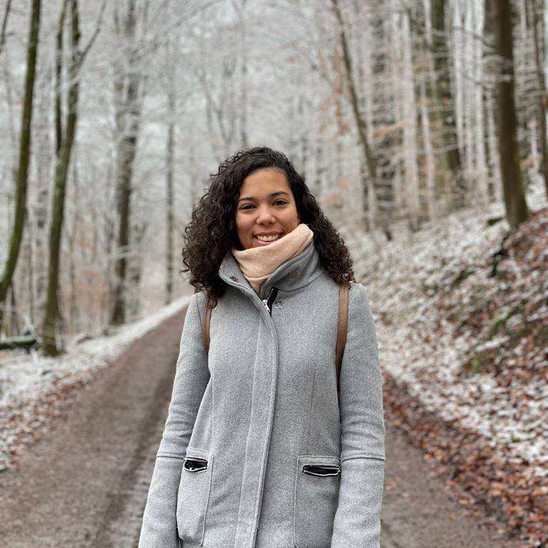 Foto van student Leraar Wiskunde in het bos met een laagje sneeuw op de bodem. Ze heeft een dikke jas aan en een dikke sjaal om.
