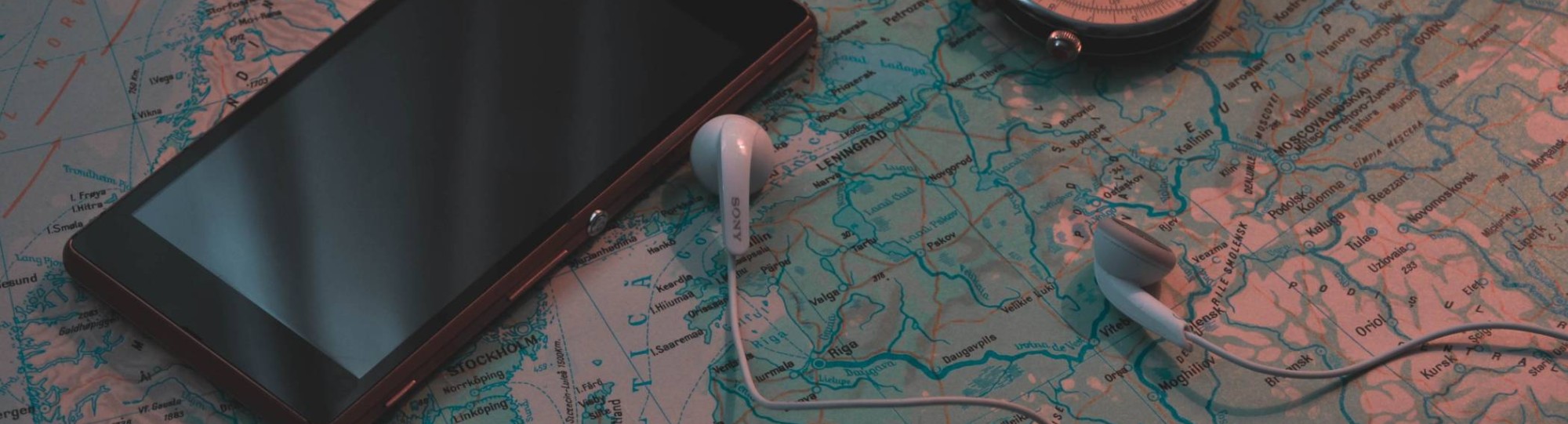 Smartphone ligt op landkaart met kompas en oordopjes