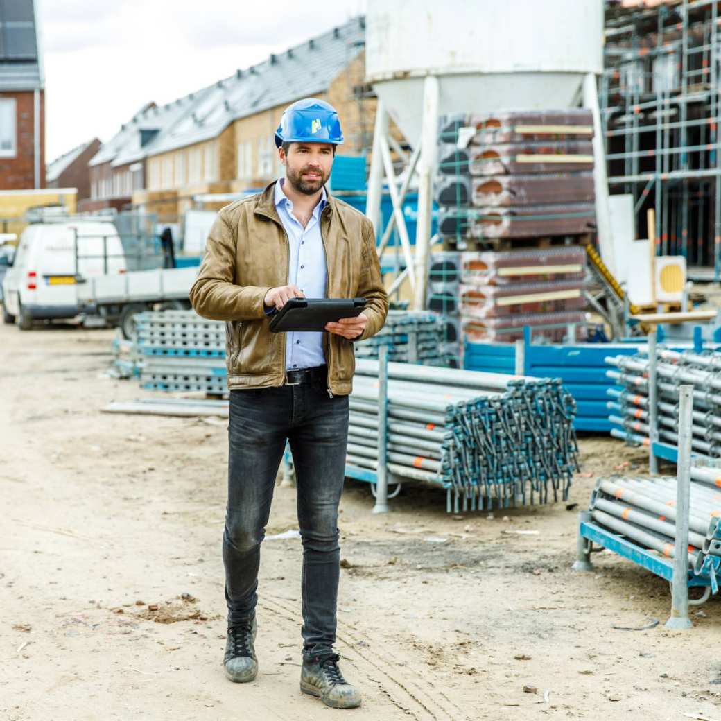 Bouwopzichter loopt met een tablet op de bouwplaats en inspecteert de vorderingen