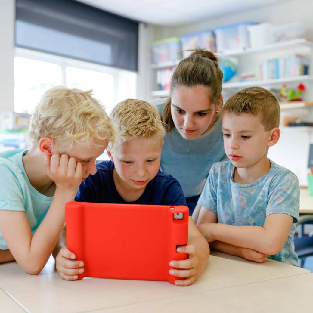 Juf met 3 schoolkinderen achter een tablet.