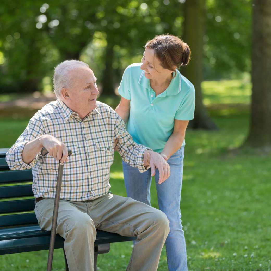 verzorger vrouw helpt senior man met stok in park