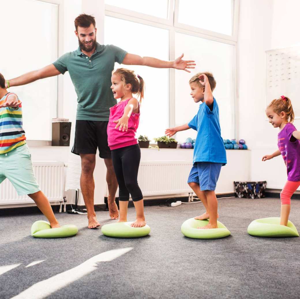 109979 kinderen wandelen op pilates-ballen tijdens training op sportschool met mannelijke coach