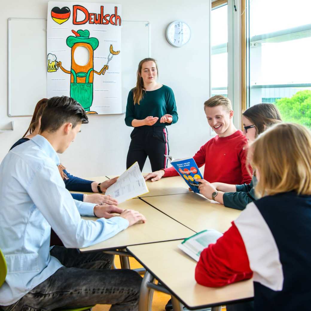 Duits docente staat voor de klas en geeft uitleg, terwijl haar vijf studenten kijken in het opdrachtenboek.