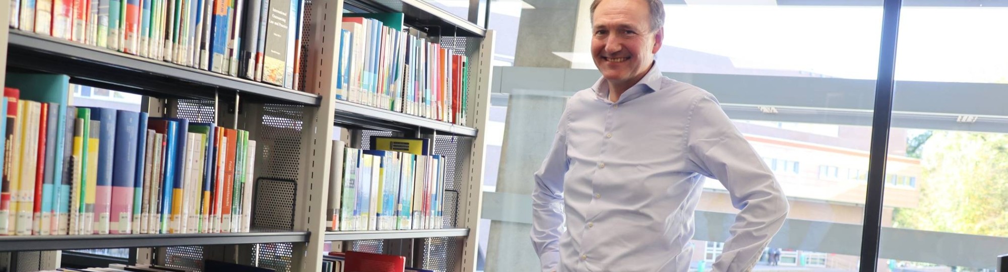 464024 Docent-onderzoeker Ger Sluman staand voor boekenkast in het studiecentrum op Ruitenberglaan 31, na een interview over zijn onderzoek.