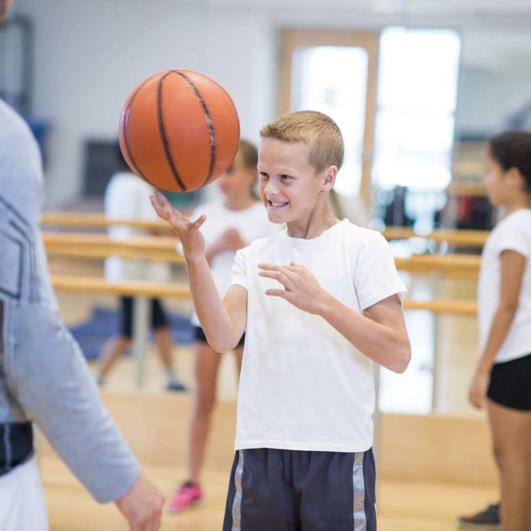 Jongen in gymzaal balanceert een basketbal op zijn vinger.