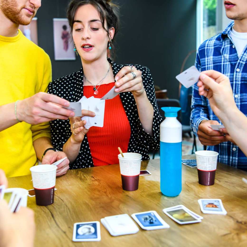 Vijf studenten spelen een kaartspel met iets te drinken erbij.