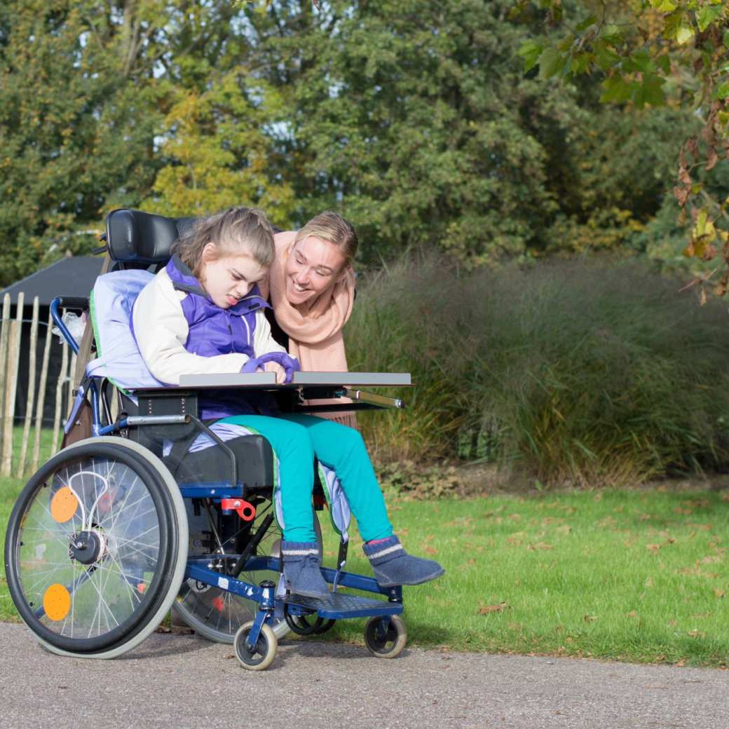 gehandicapt kind in een rolstoel buiten ontspannen samen met een verzorger