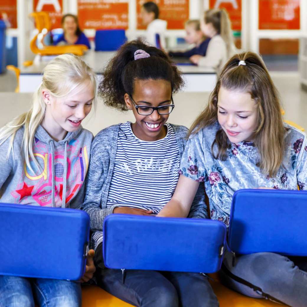 Drie kinderen zitten op een rijtje achter hun laptop met blauwe hoes.