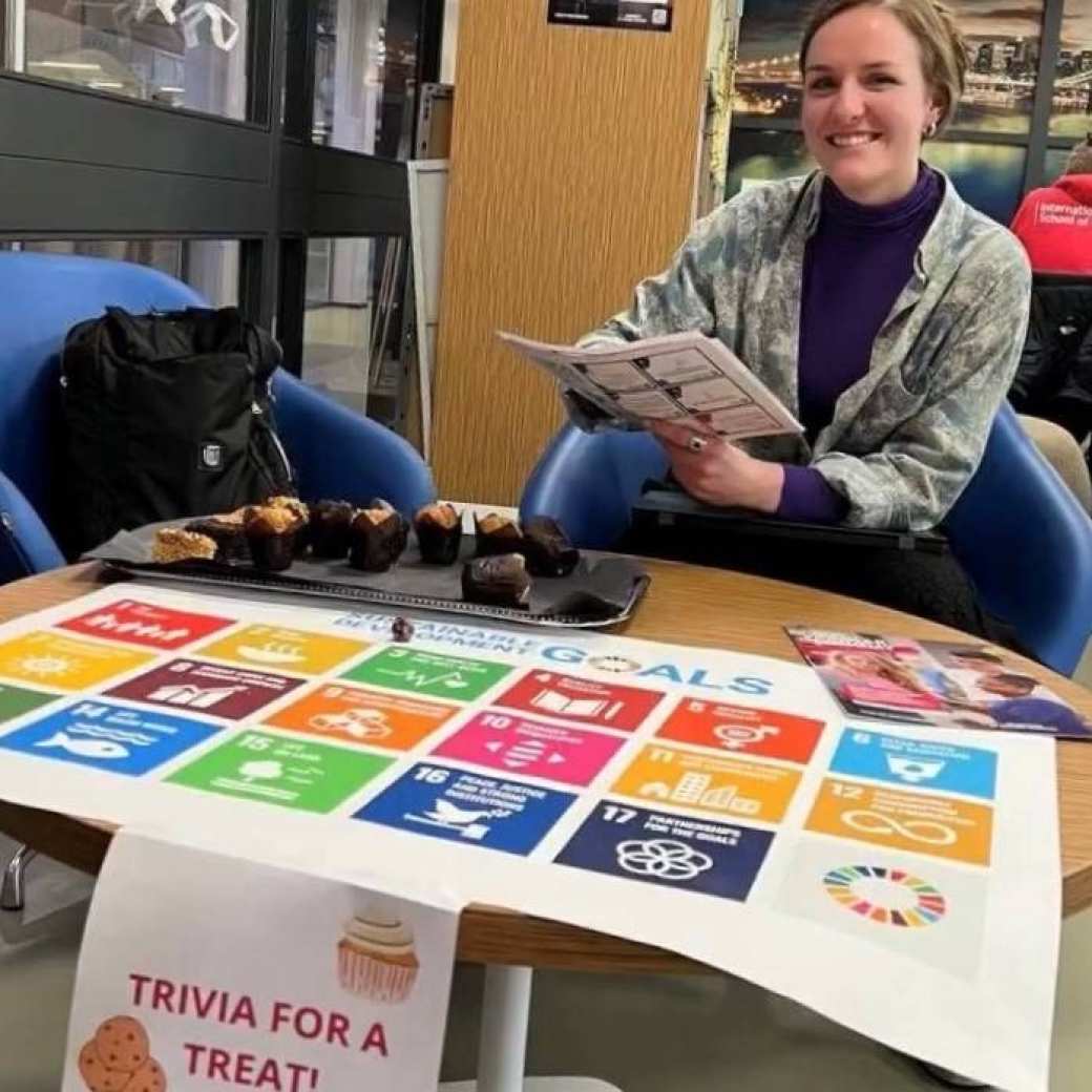 Angela Piccioni sits at a table, with muffins and a large printout of the SDGs.
