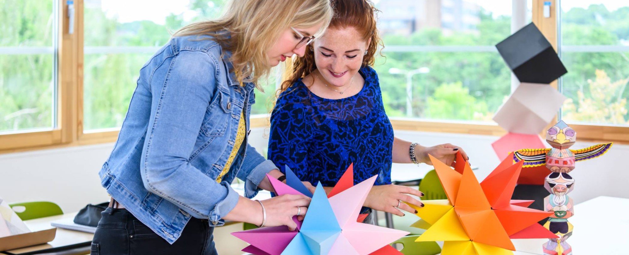Twee studenten maken in een klaslokaal een papieren ster met allemaal verschillende kleuren.
