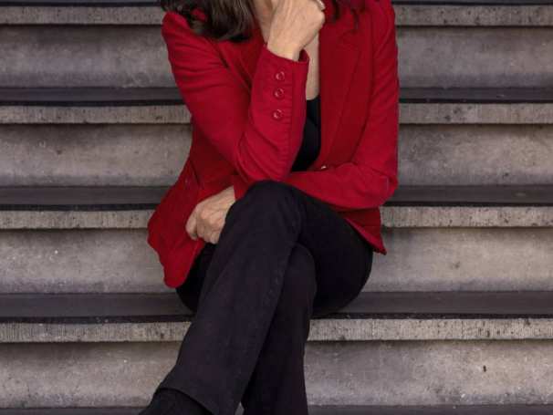 559904 Campustheater. Debby Petters zit op een trap. Ze heeft een rood jasje aan.